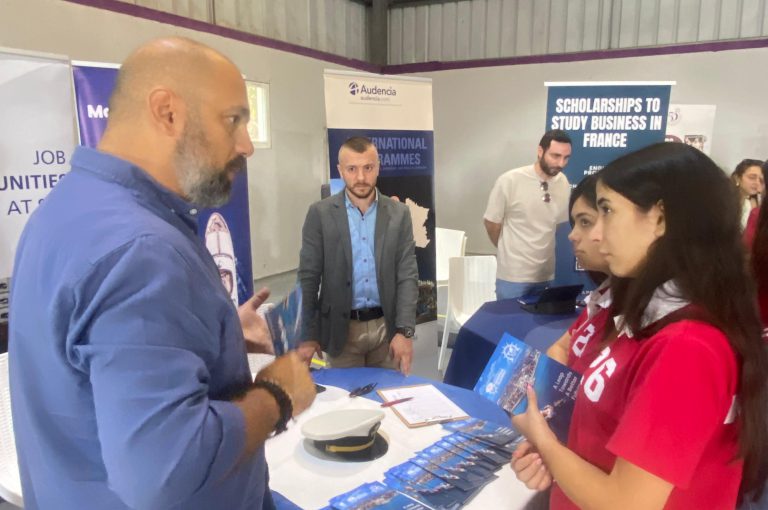 High school students in Grades 10–-12 visiting a university fair, exploring booths and talking to representatives.