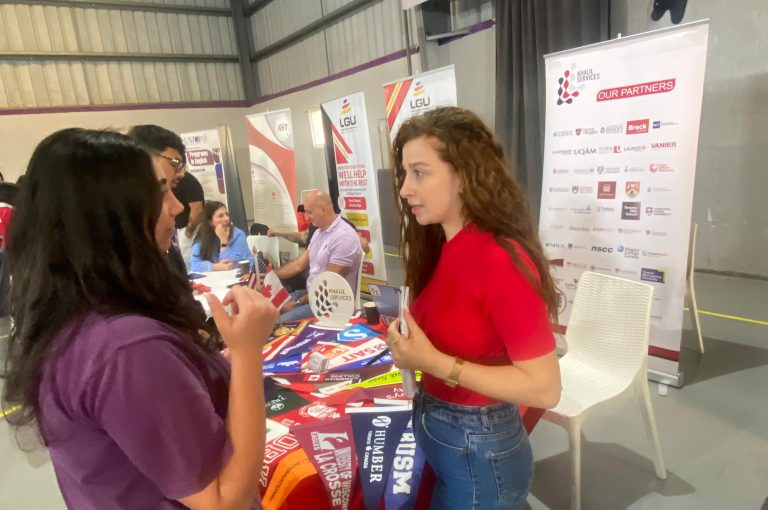 High school students in Grades 10–-12 visiting a university fair, exploring booths and talking to representatives.