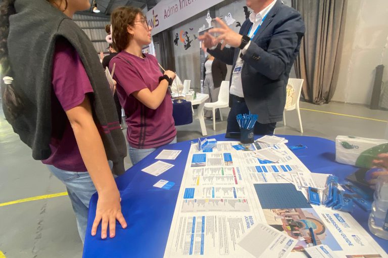 High school students in Grades 10–-12 visiting a university fair, exploring booths and talking to representatives.