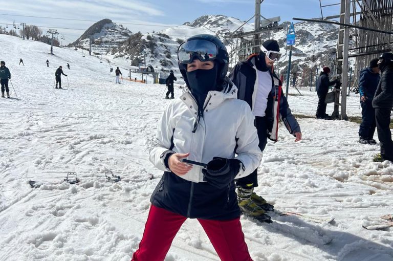 Students skiing and playing in the snow on a mountain during a school trip, with a bright winter landscape in the background.