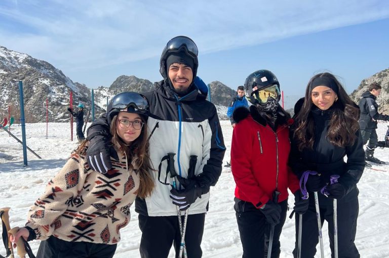 Students skiing and playing in the snow on a mountain during a school trip, with a bright winter landscape in the background.