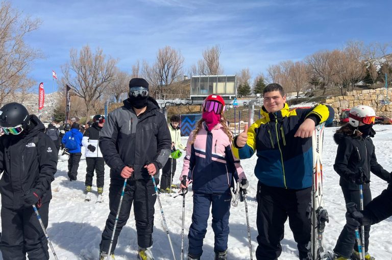 Students skiing and playing in the snow on a mountain during a school trip, with a bright winter landscape in the background.