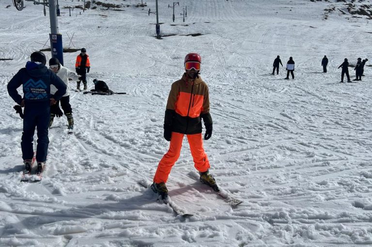 Students skiing and playing in the snow on a mountain during a school trip, with a bright winter landscape in the background.